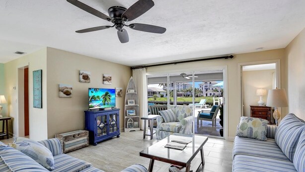 A spacious living room with a ceiling fan, a television, and a view of a pool and outdoor seating area. - Inviting Waterfront Home With Western Exposure (Marco Island)