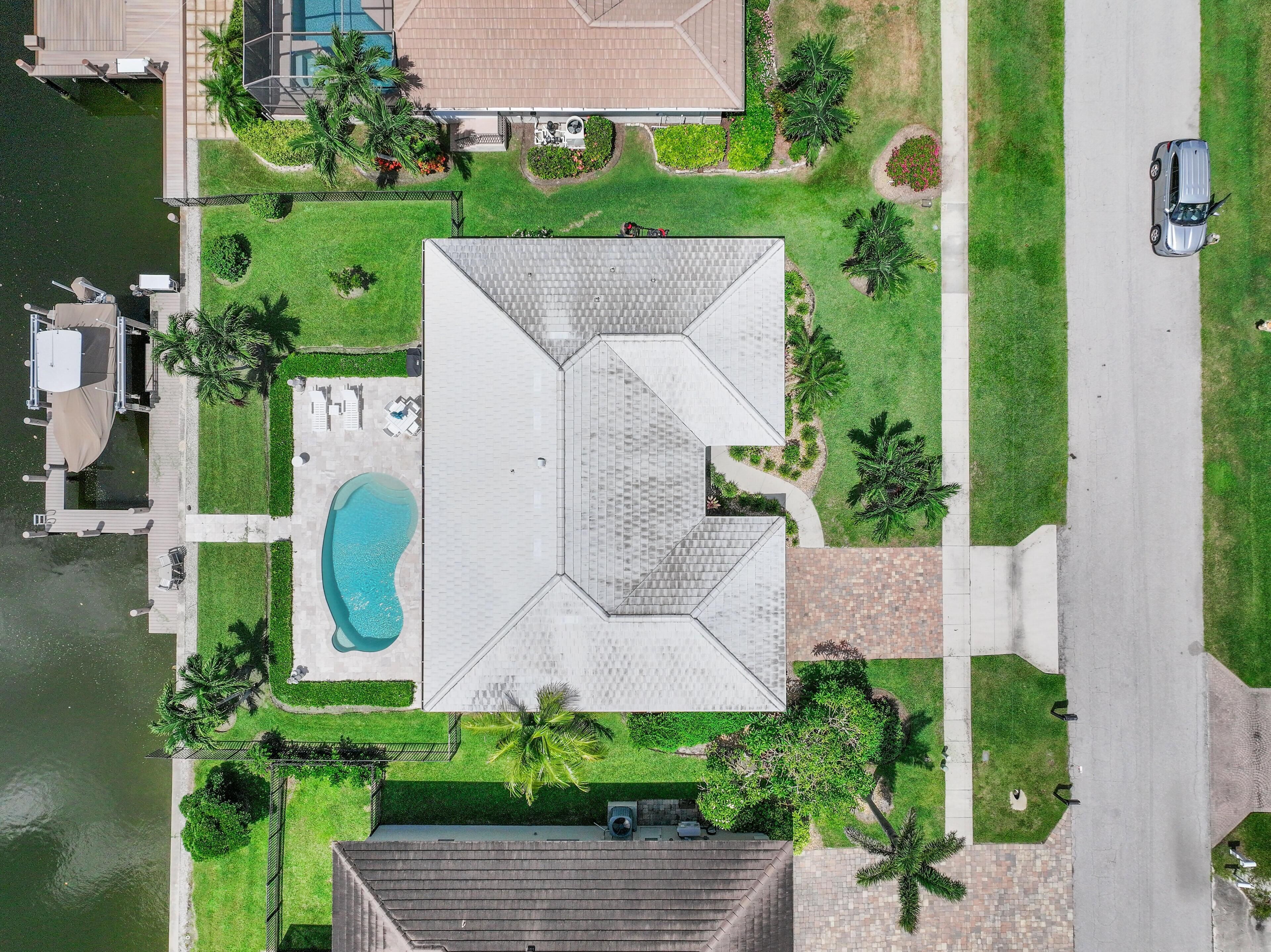 An aerial view of a residential property with a swimming pool, a covered patio, and a large lawn.