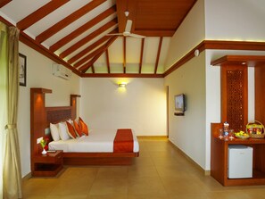 A hotel room with a bed, bedside table, nightstand, ceiling fan, TV, and a small refrigerator.