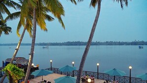 A deck with tables and chairs, umbrellas, and a view of the water. - Sea Lagoon Health Resort (Cochin)