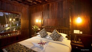 A wooden-paneled room with a bed, two wall sconces, a nightstand, and a window overlooking a garden. - Sea Lagoon Health Resort (Cochin)