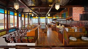 A restaurant with a long wooden bench seating area, a bar with stools, and a view through large windows. - Sea Lagoon Health Resort (Cochin)
