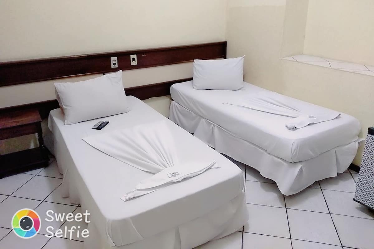 Two single beds with white linens and pillows, a wooden headboard, and a tiled floor.