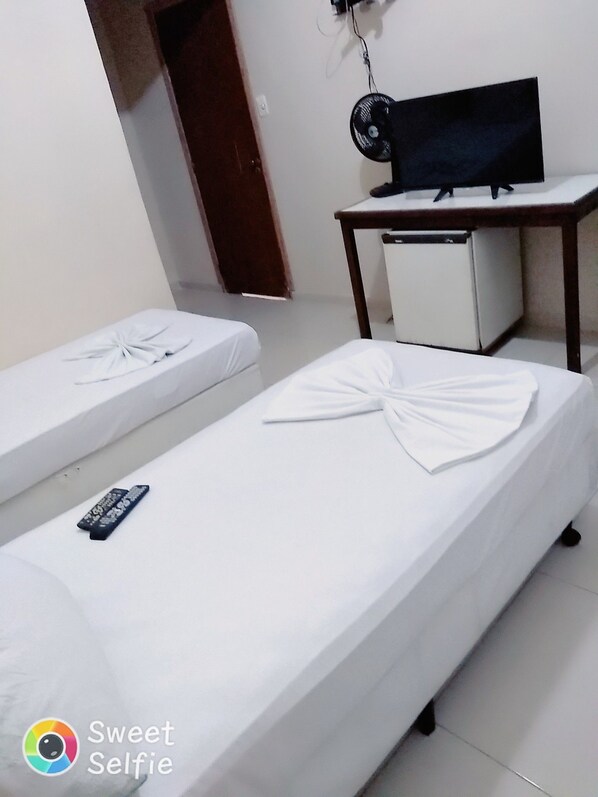 A hotel room with two single beds, a small table with a TV, and a door leading to another room. - Hotel Central Rosário (Jundiai)