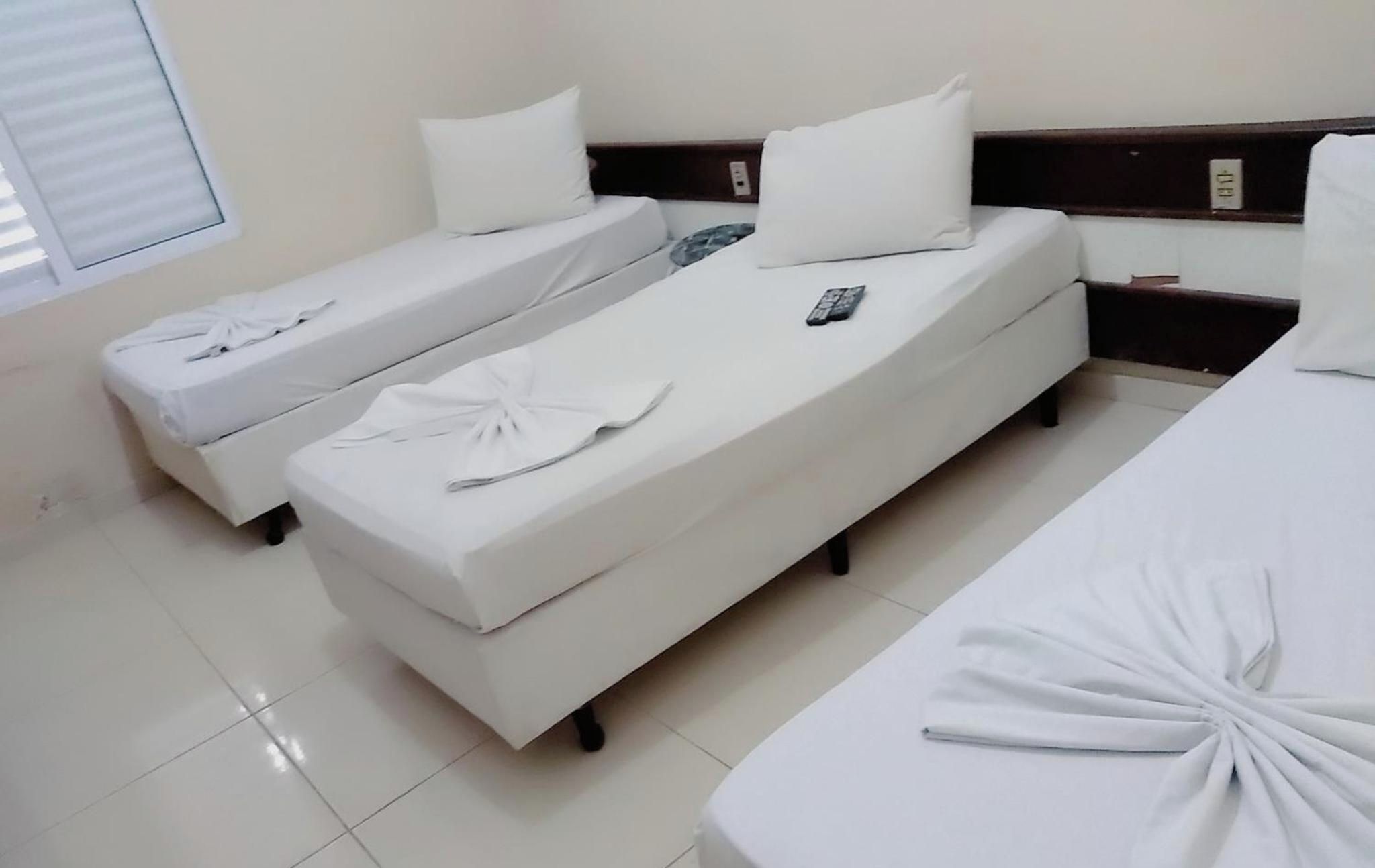 Quarto de hotel com duas camas de solteiro, cada uma com colchão e travesseiro brancos, e um controle remoto sobre a cama.
