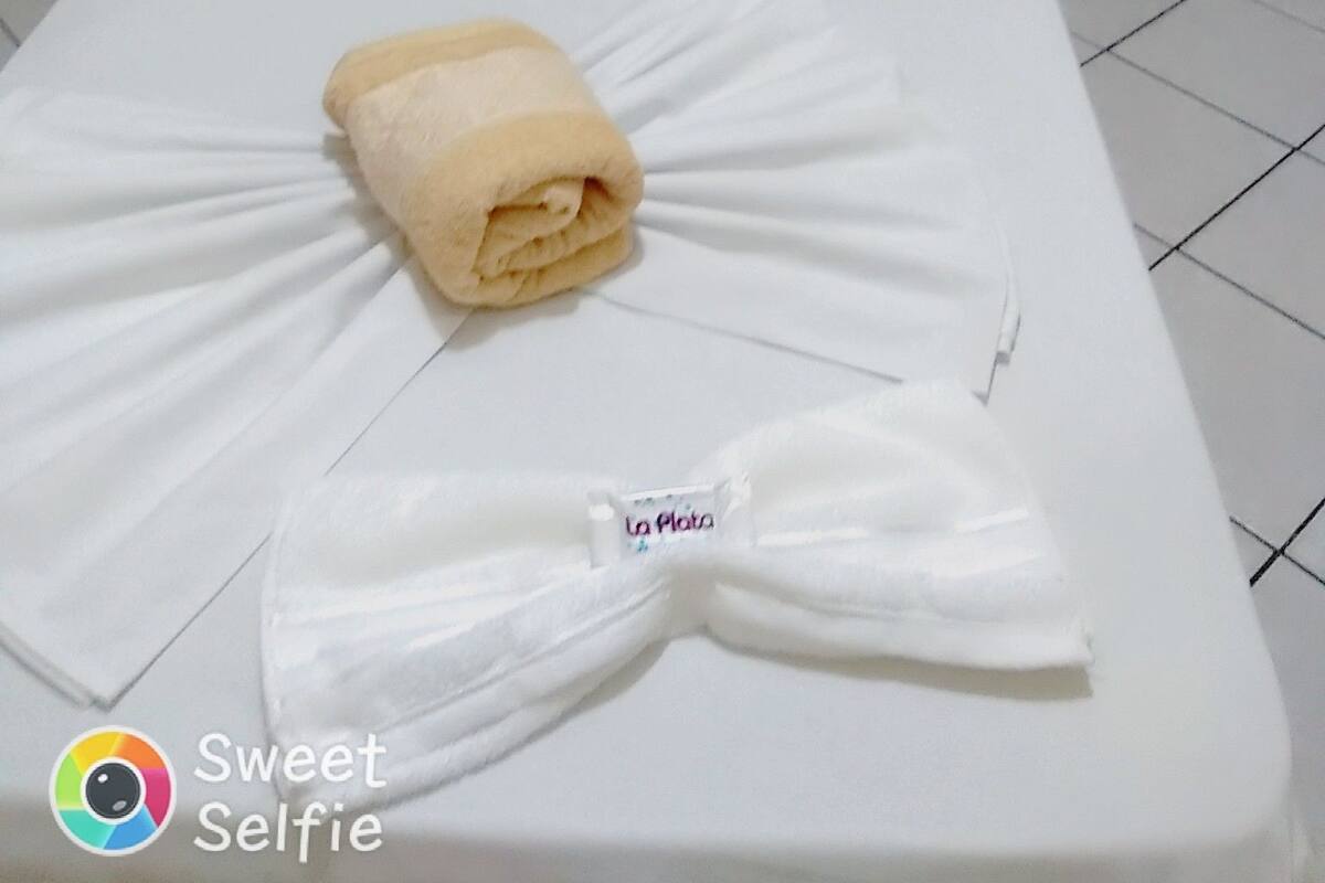 A neatly made bed with a rolled towel and a folded towel on a white mattress in a hotel room.
