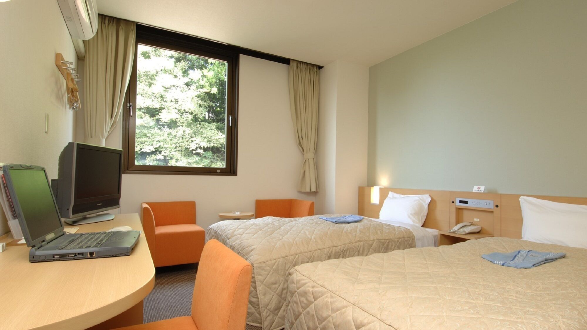 A hotel room with two beds, a desk with a laptop, a chair, and a window with curtains.