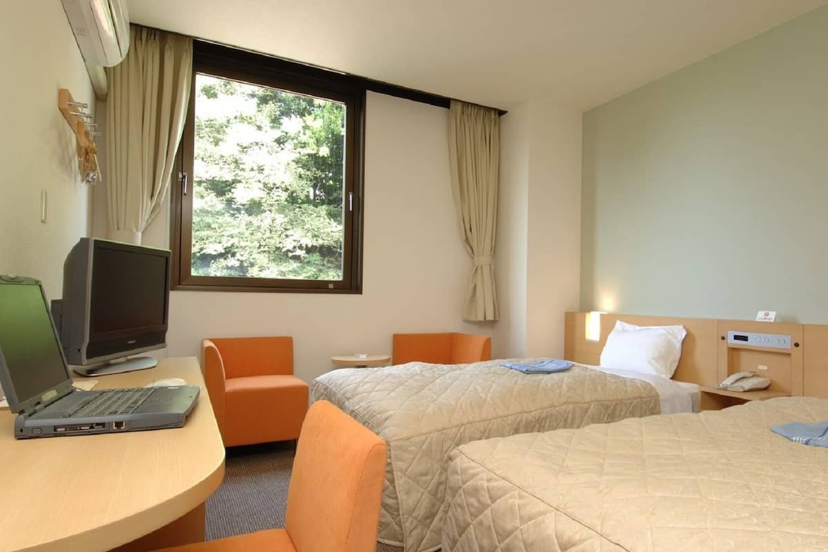 A hotel room with two beds, a desk with a laptop, a chair, and a window with curtains.