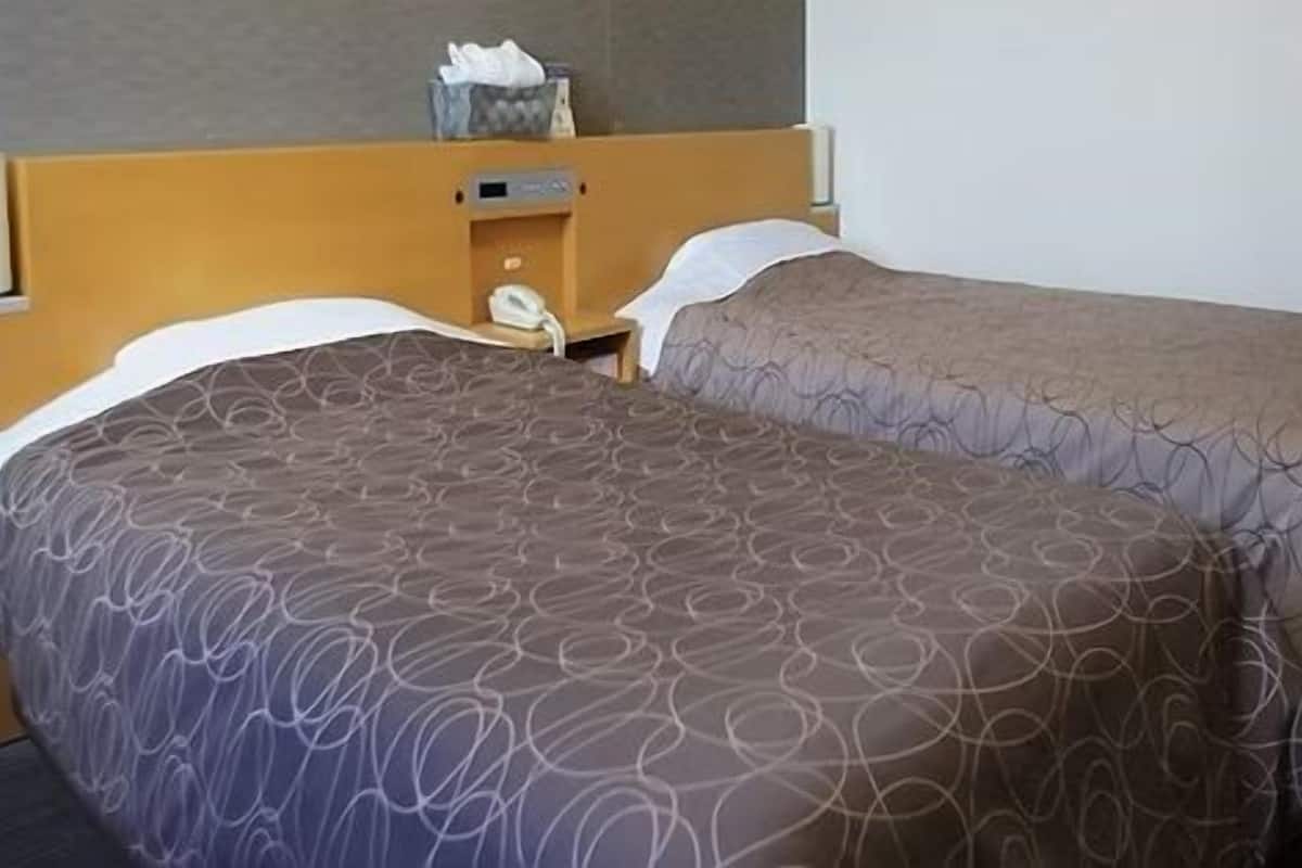 Un lit double avec une literie à motifs, une tête de lit en bois, une table de chevet avec une lampe et une poubelle.