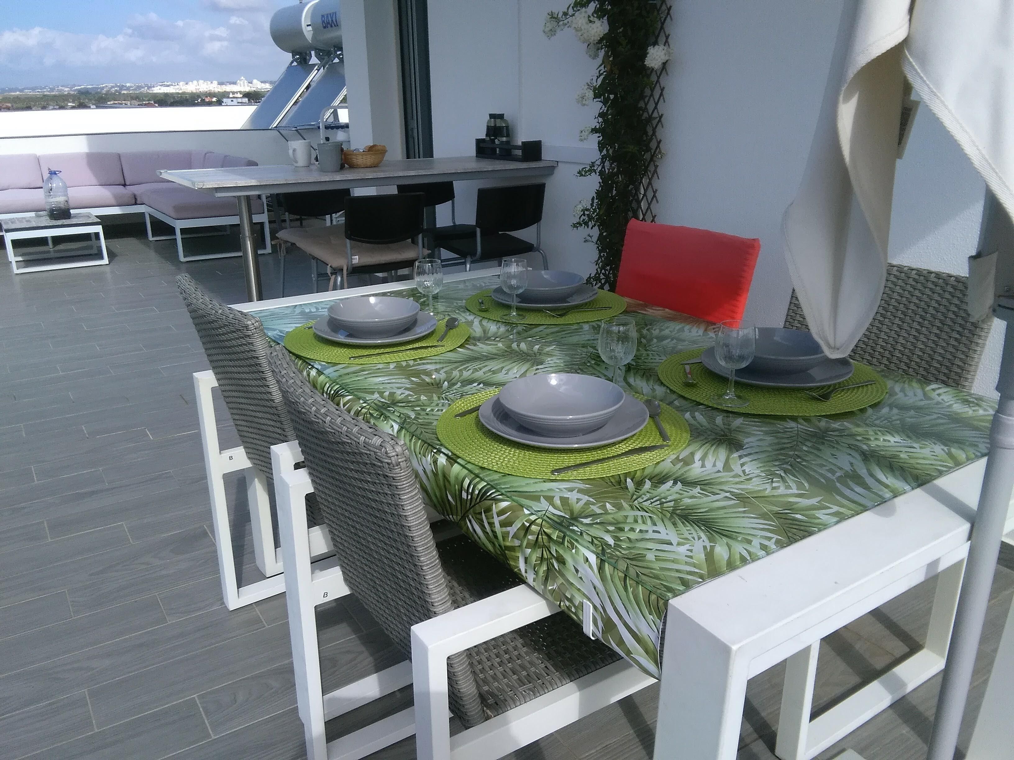 A rooftop terrace with a dining table set for four, surrounded by wicker chairs.
