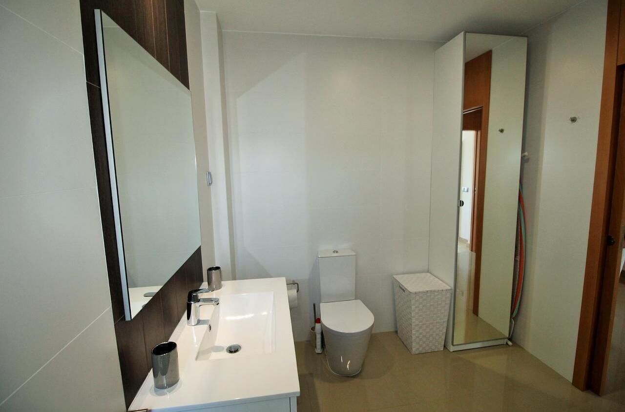 Un baño moderno con lavamanos, espejo, inodoro y un cubo de basura.
