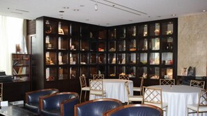 A modern dining area with leather chairs, round tables, and a dark wooden bookshelf filled with items. - Mizusawa Grand Hotel (Oshu)