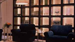 A room with two dark sofas, a small table with a vase of flowers, and a wall with illuminated shelves. - Mizusawa Grand Hotel (Oshu)