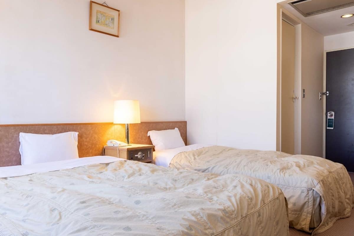 A hotel room with two beds, a nightstand with a lamp, and a door.