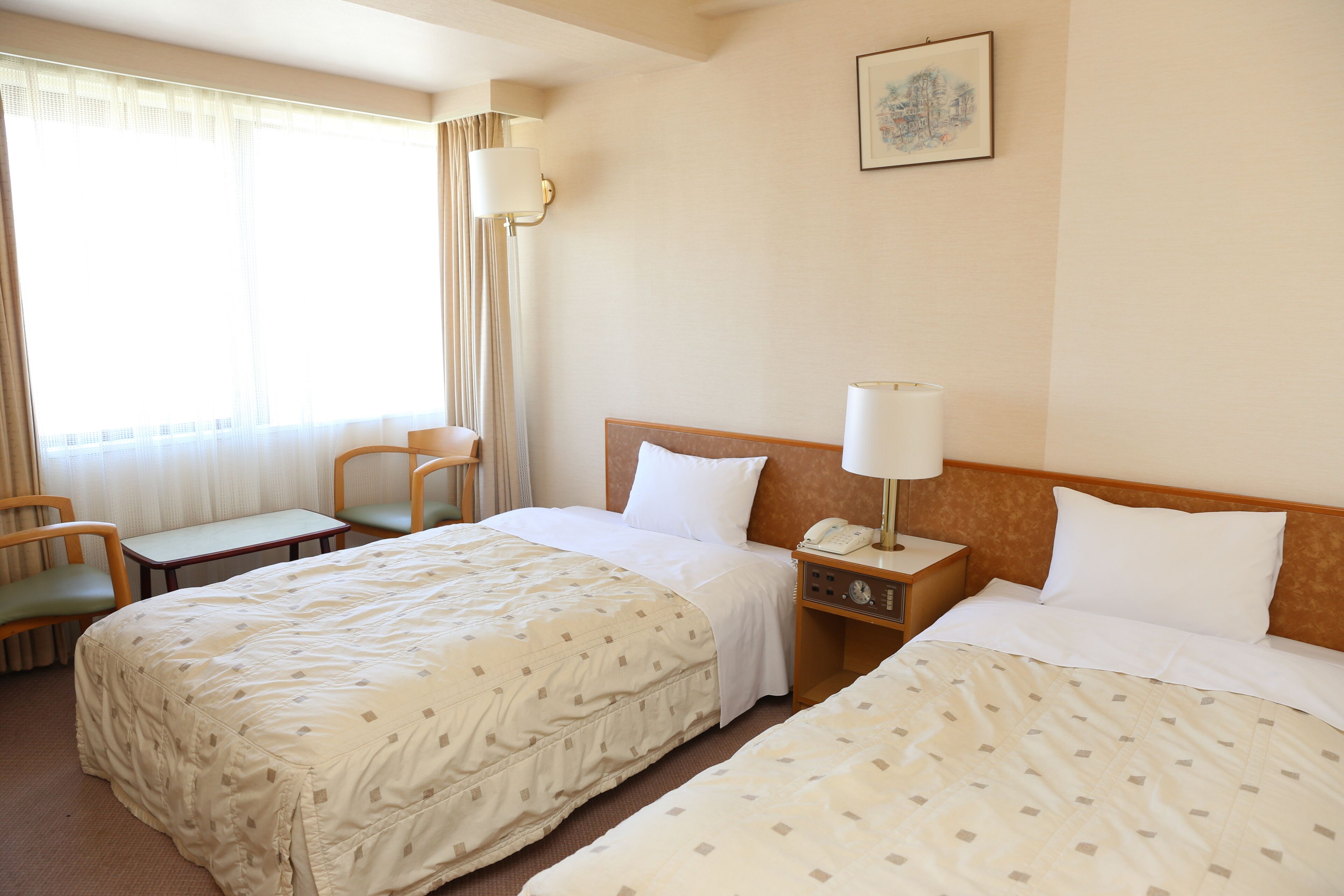 A hotel room with two beds, a desk, a chair, a nightstand with a lamp, and a painting on the wall.