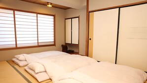 A traditional Japanese room with tatami flooring, a large bed with white bedding, a sliding door, and a window with shoji screens. - Mizusawa Grand Hotel (Oshu)