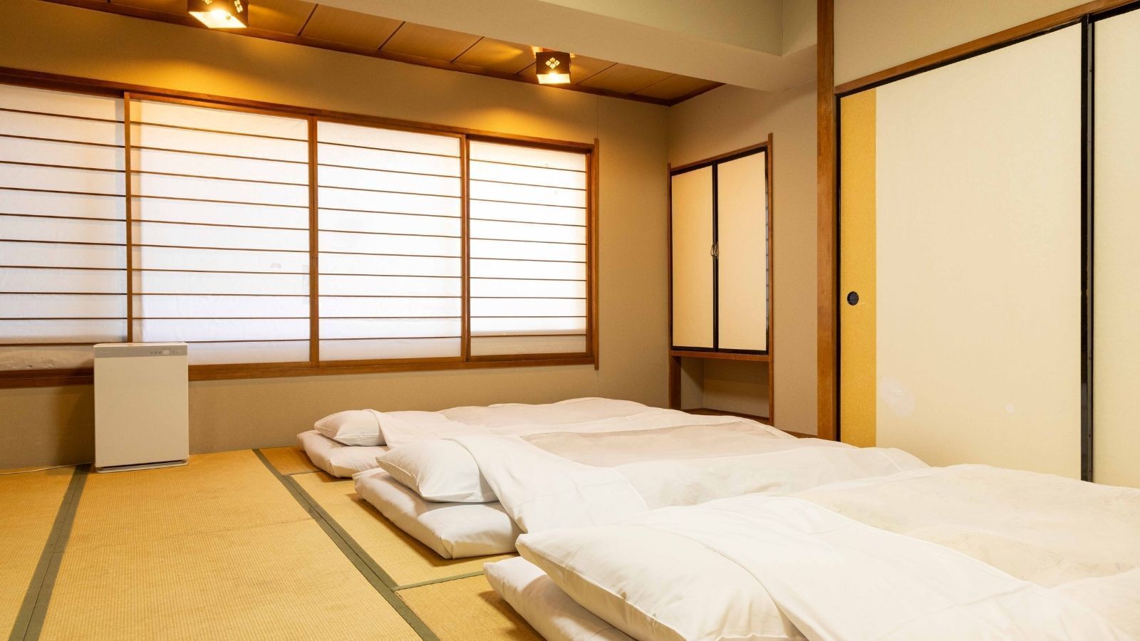 A traditional Japanese-style room with tatami flooring, a futon bed, a small desk, and sliding doors.