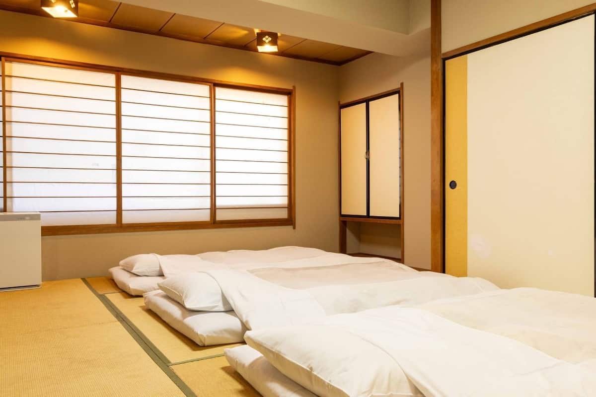 Um quarto em estilo tradicional japonês, com tatames no chão, futon como cama, uma pequena escrivaninha e portas deslizantes.