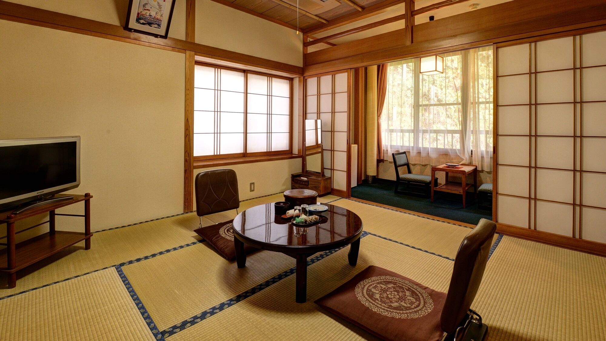 A traditional Japanese room with tatami flooring, a tatami mat table, a television, and sliding doors.