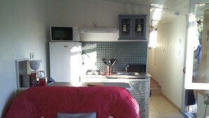 A compact kitchen with a microwave, stove, and cabinets. A bed with patterned pillows is visible in the foreground. - shed in a property close to the countryside (Pélissanne)