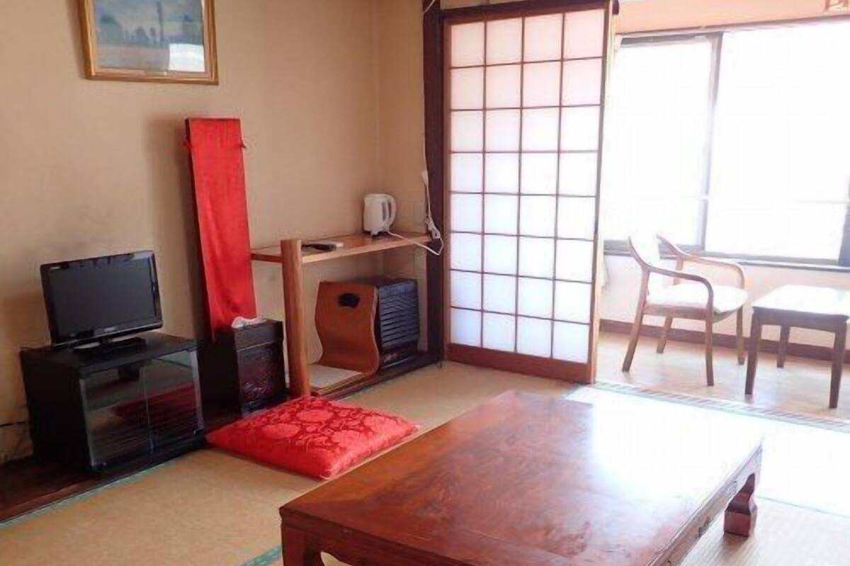 A traditional Japanese room with tatami flooring, a wooden table, a television, and a sliding door.