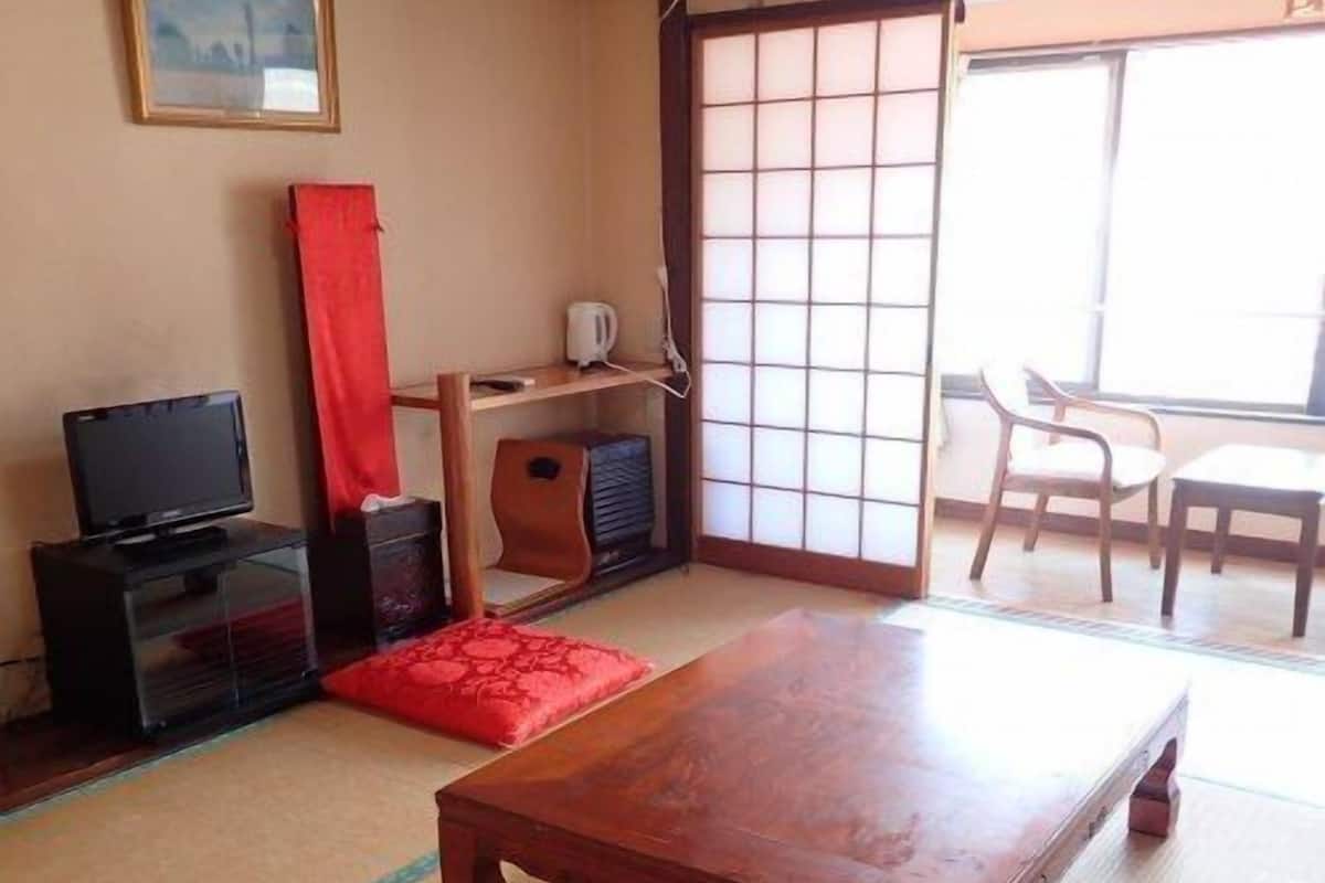 Perinteinen japanilainen huone, jossa on tatamimatto, puinen pöytä, televisio ja liukuovi.
