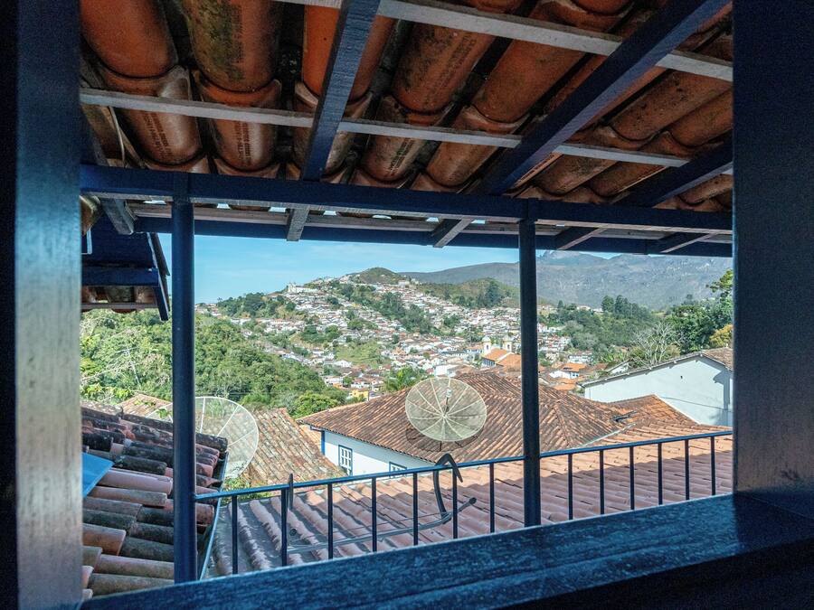 A view from a balcony with a tiled roof and metal railing, overlooking a town with houses and hills.