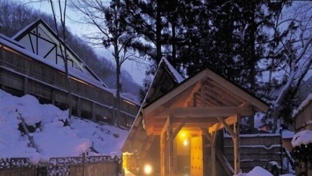 Une cabane en bois dotée d’un porche abrité, entourée d’un paysage enneigé et d’arbres.