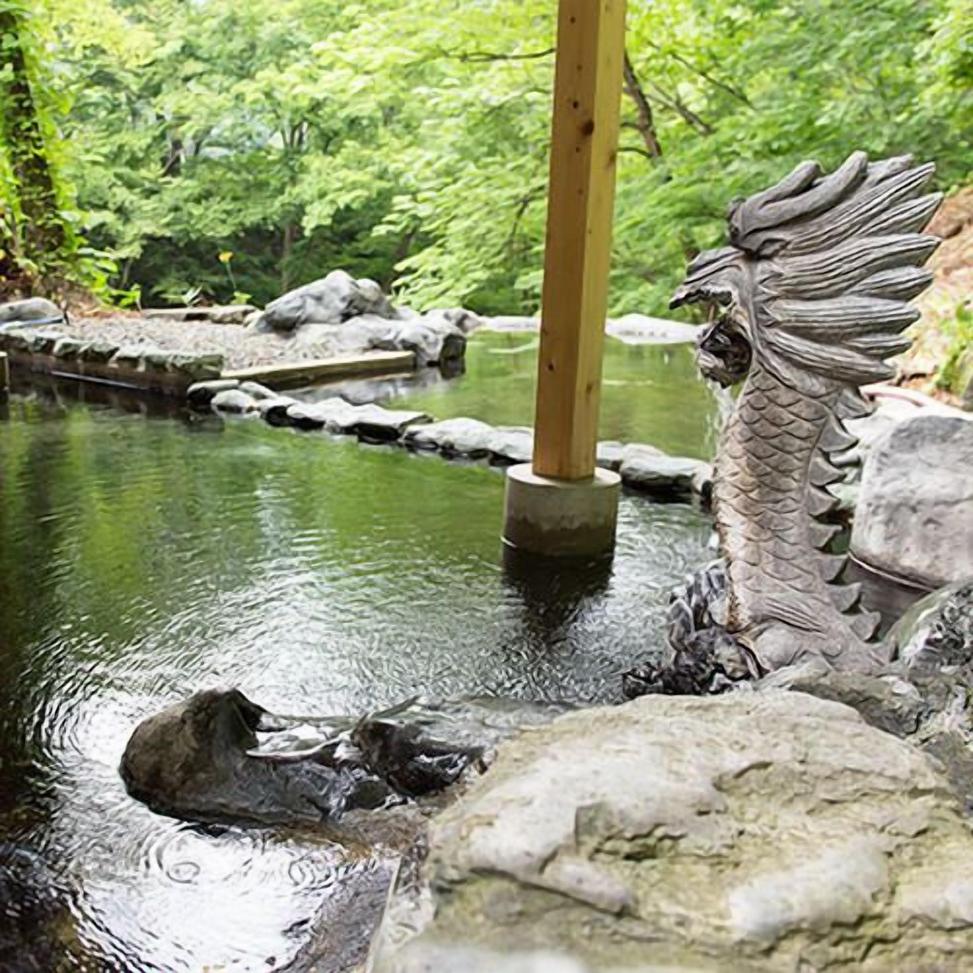 A dragon statue in a water feature with rocks and greenery in the background.