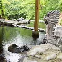Una estatua de dragón en un elemento acuático con rocas y follaje de fondo.