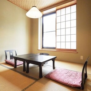 A traditional Japanese room with tatami flooring, a low table, a chair, and a window with shoji screens.