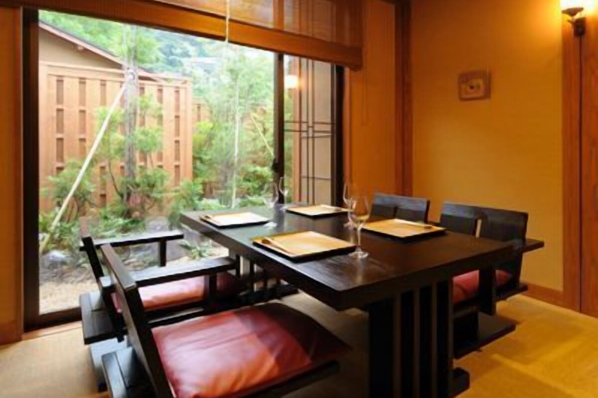 Un comedor con una larga mesa y bancos, ventanas amplias y vistas al verde exterior.