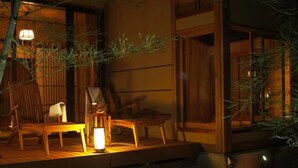 A traditional Japanese-style room with tatami flooring, a low table, and a chair. There is a lamp on the table and a window with a view of the outside. - Minakami Onsen Bettei Yaeno (Minakami)