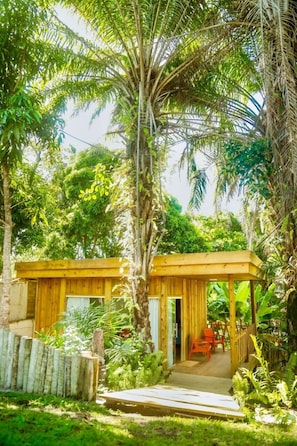 A wooden cabin with a porch, surrounded by lush greenery and tall trees. - Casa Jequitibá Rosa (Porto Seguro)