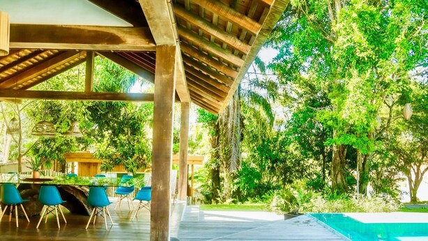 An outdoor covered area with a pool, wooden deck, and blue chairs. - Casa Jequitibá Rosa (Porto Seguro)