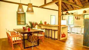 A rustic kitchen with wooden floors, a dining table with chairs, hanging lights, and a bar area. - Casa Jequitibá Rosa (Porto Seguro)