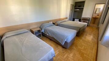 Habitació d'hotel amb tres llits individuals, un terra de fusta, un armari i una taula petita amb una cadira.
