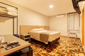 A hotel room with a bed, bedside table, and a desk with a chair.