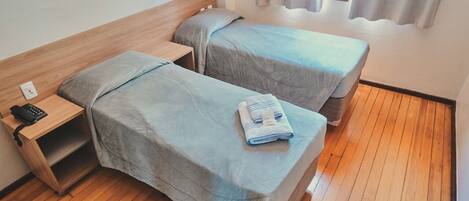 Una habitación con dos camas, una mesita de noche con teléfono y una ventana con cortinas.