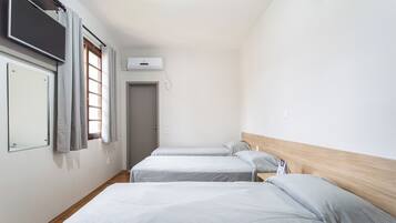 Quarto de hotel com duas camas de solteiro, uma televisão de tela plana na parede, uma janela com cortinas e uma porta.