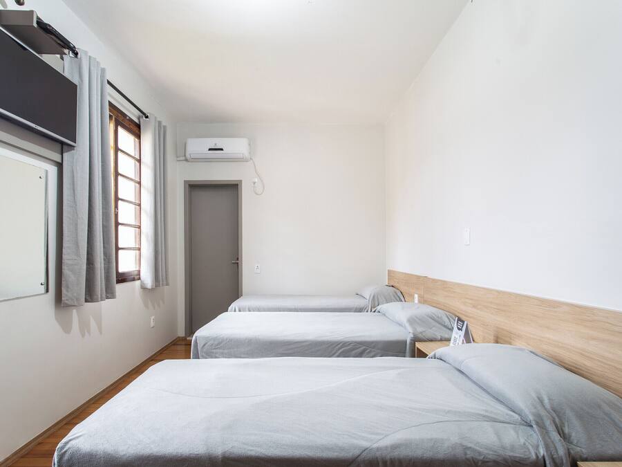 Quarto de hotel com duas camas de solteiro, uma televisão de tela plana na parede, uma janela com cortinas e uma porta.