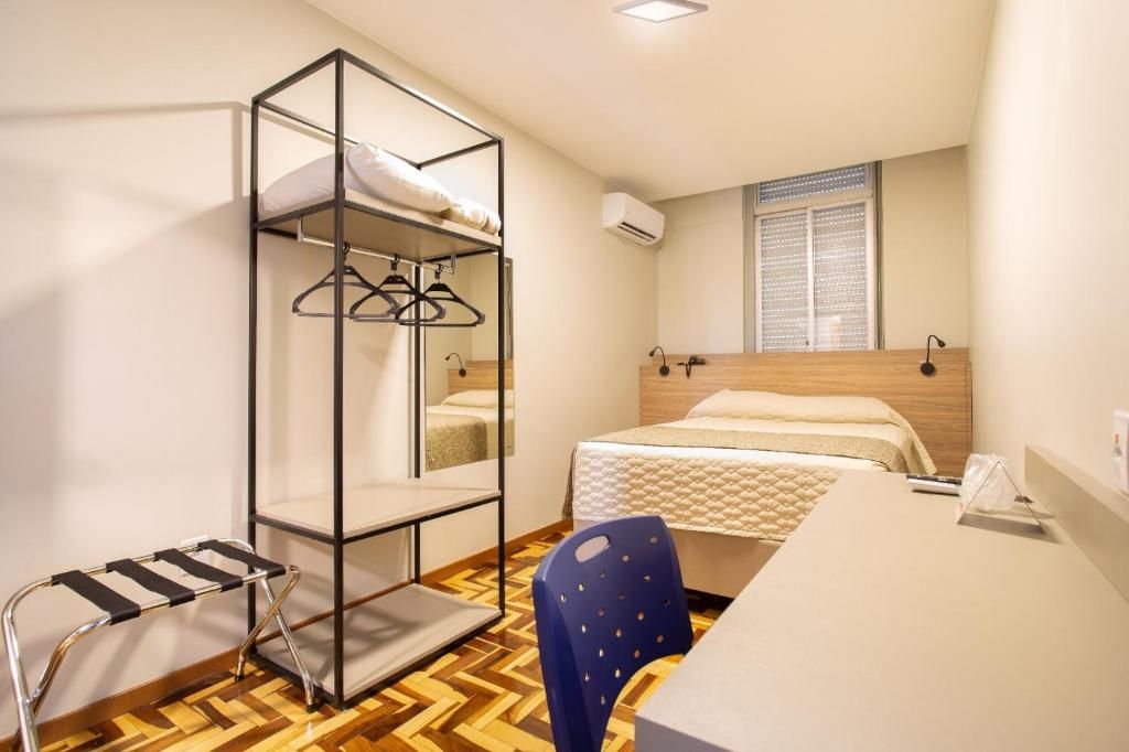 A room with a bunk bed, a desk with a chair, a hanging rack, and a window with blinds.