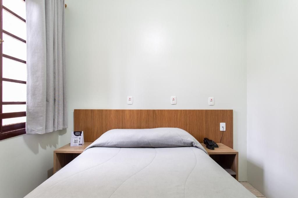 A single bed with a wooden headboard, a bedside table with a phone, and a window with curtains.