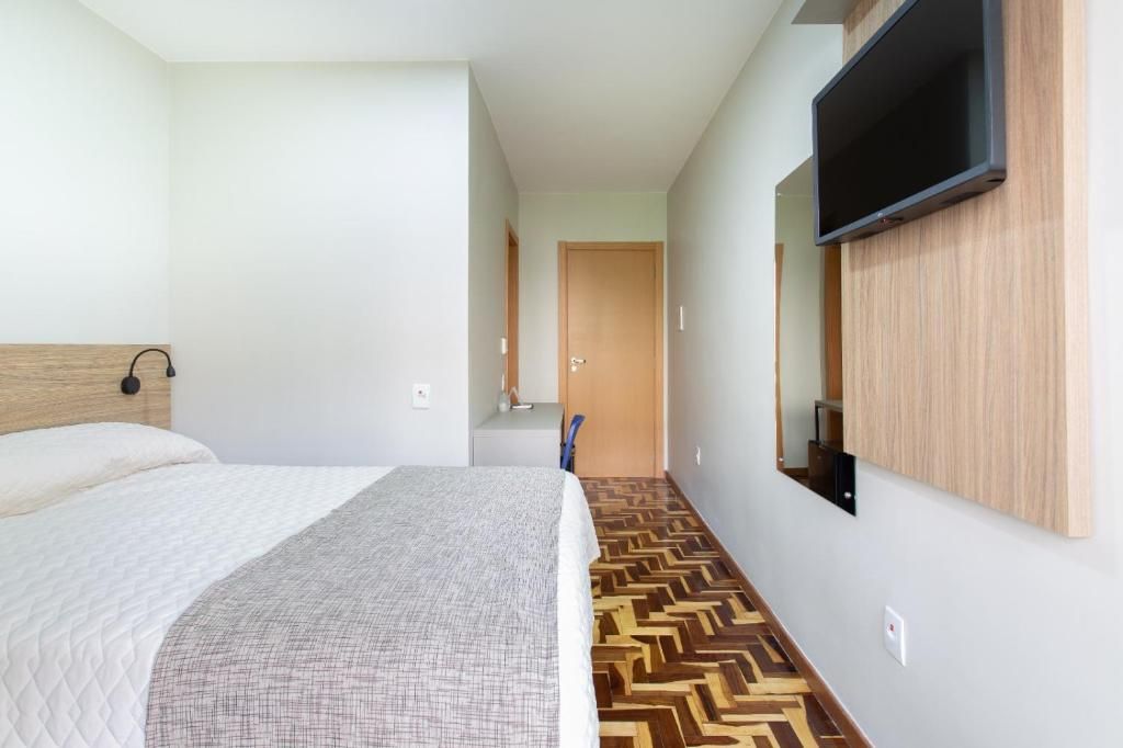 A bedroom with a bed, a television mounted on the wall, and a patterned floor.