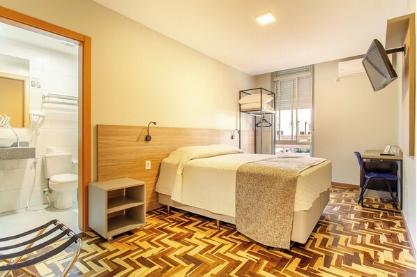 A hotel room with a bed, a desk, a chair, a small shelf, and a bathroom visible through an open door. - Hotel Dom Rafael Business (Santa Maria)