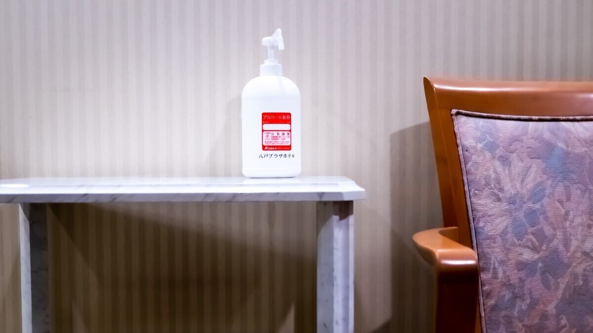 A white bottle with a pump dispenser on a small table next to a wooden chair with a floral pattern.