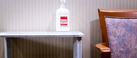A white bottle with a pump dispenser on a small table next to a wooden chair with a floral pattern.