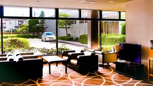 Un hall d’hôtel doté d’une grande fenêtre, d’un espace salon et d’un téléviseur.