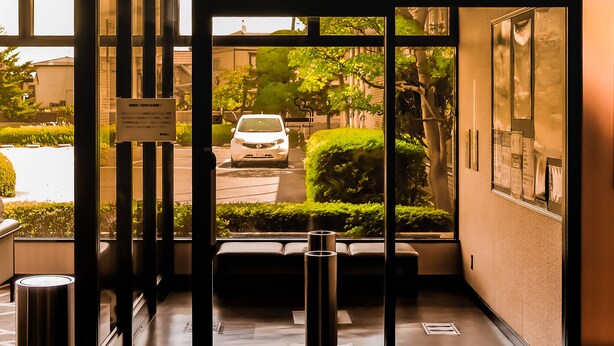 L’entrée d’un hôtel, avec un banc, un panneau indiquant un espace réservé aux fumeurs, et une vue sur une voiture garée à l’extérieur.