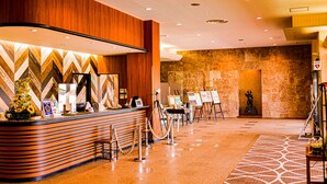 Un espace d’accueil d’hôtel avec un comptoir de réception en bois, un mur orné d’un motif en chevrons et une statue en arrière-plan.